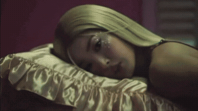 A Woman With Long Blonde Hair Is Laying On A Bed GIF