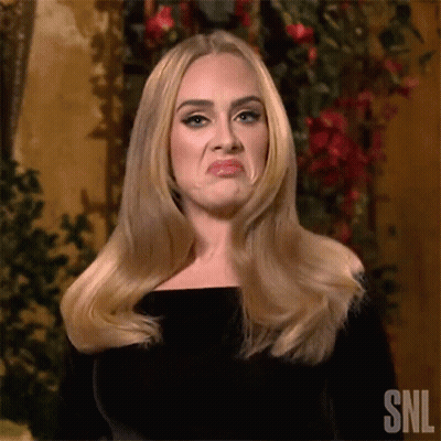 A Woman With Long Blonde Hair Is Making A Funny Face While Standing In Front Of Flowers . GIF