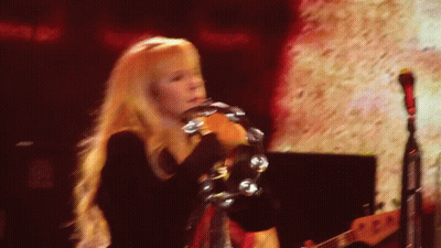 A Woman With Long Blonde Hair Is Playing A Tambourine On A Stage GIF