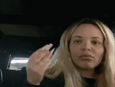 A Woman With Long Blonde Hair Is Sitting In The Back Seat Of A Car And Making A Funny Face . GIF