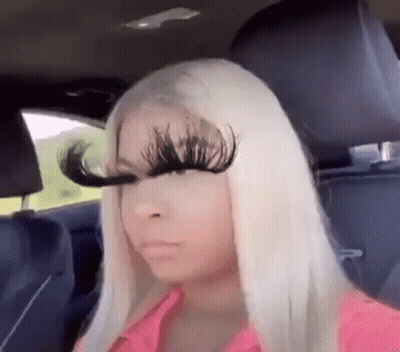 A Woman With Long Blonde Hair Is Sitting In The Back Seat Of A Car With A Pair Of Fake Eyelashes On Her Face . GIF