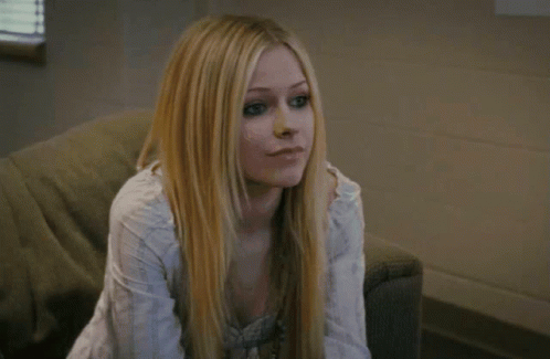 A Woman With Long Blonde Hair Is Sitting On A Couch Looking At The Camera GIF