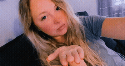 A Woman With Long Blonde Hair Is Sitting On A Couch Taking A Selfie . GIF