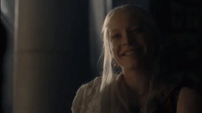 A Woman With Long Blonde Hair Is Smiling And Looking At The Camera . GIF