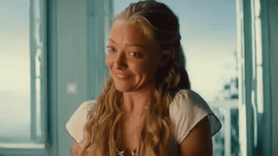 A Woman With Long Blonde Hair Is Smiling And Looking Out Of A Window GIF