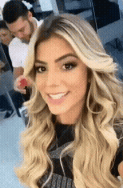 A Woman With Long Blonde Hair Is Smiling And Taking A Selfie GIF