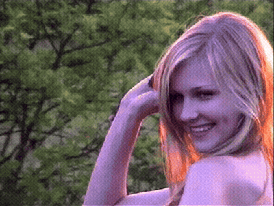 A Woman With Long Blonde Hair Is Smiling In Front Of A Tree GIF