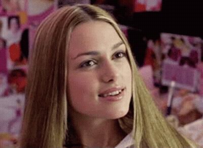 A Woman With Long Blonde Hair Is Smiling In Front Of A Wall Of Pictures GIF