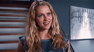 A Woman With Long Blonde Hair Is Smiling In Front Of Stairs And A Painting GIF