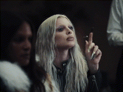 A Woman With Long Blonde Hair Is Smoking A Cigarette In A Dark Room GIF