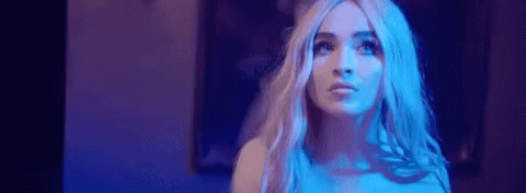 A Woman With Long Blonde Hair Is Standing In A Dark Room With Blue Lights . GIF