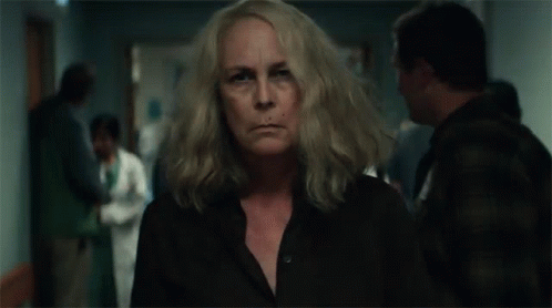 A Woman With Long Blonde Hair Is Standing In A Hospital Hallway . GIF