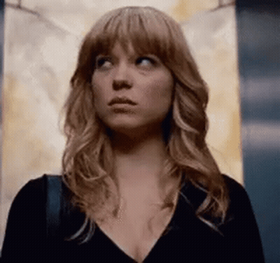 A Woman With Long Blonde Hair Is Standing In An Elevator Looking Up . GIF