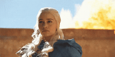 A Woman With Long Blonde Hair Is Standing In Front Of A Large Fire GIF