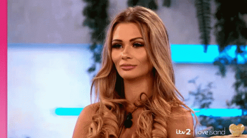A Woman With Long Blonde Hair Is Standing In Front Of A Love Island Sign GIF
