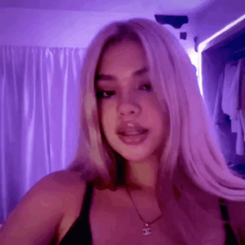 A Woman With Long Blonde Hair Is Standing In Front Of A Purple Wall . GIF