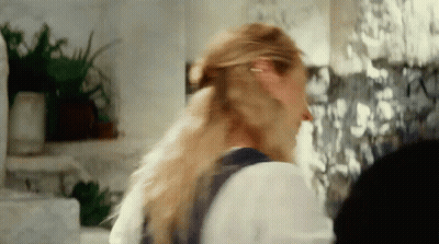 A Woman With Long Blonde Hair Is Standing In Front Of A Wall With Pictures On It GIF
