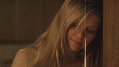 A Woman With Long Blonde Hair Is Standing Next To A Wooden Wall . GIF