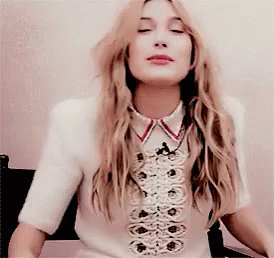 A Woman With Long Blonde Hair Is Wearing A White Shirt With A Red Collar GIF