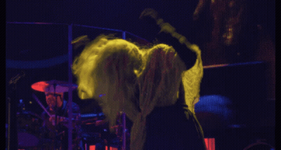 A Woman With Long Blonde Hair Stands In Front Of A Drummer On A Stage GIF