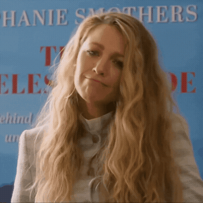 A Woman With Long Blonde Hair Stands In Front Of A Sign That Says Hanie Smothers GIF