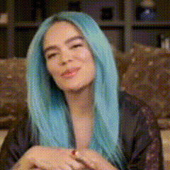 A Woman With Long Blue Hair Is Sitting On A Couch . GIF
