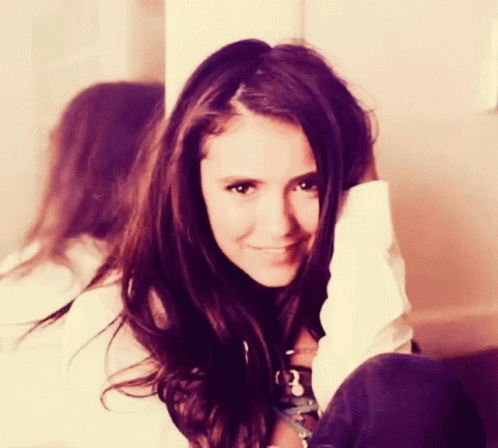 A Woman With Long Brown Hair And A White Shirt Smiles For The Camera GIF