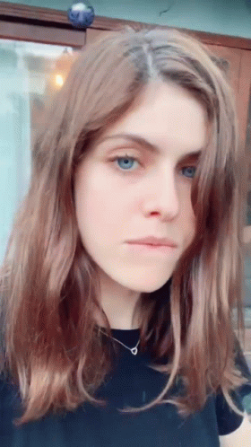 A Woman With Long Brown Hair And Blue Eyes Is Wearing A Black Shirt . GIF