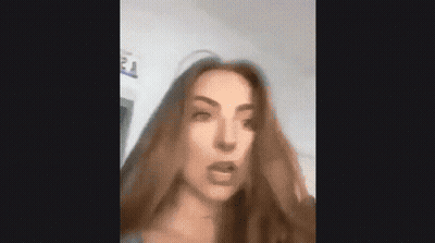 A Woman With Long Brown Hair Is Making A Funny Face And Looking At The Camera . GIF