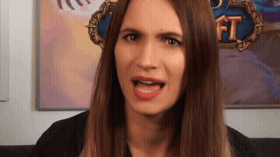 A Woman With Long Brown Hair Is Making A Funny Face In Front Of A Painting Of A Game . GIF