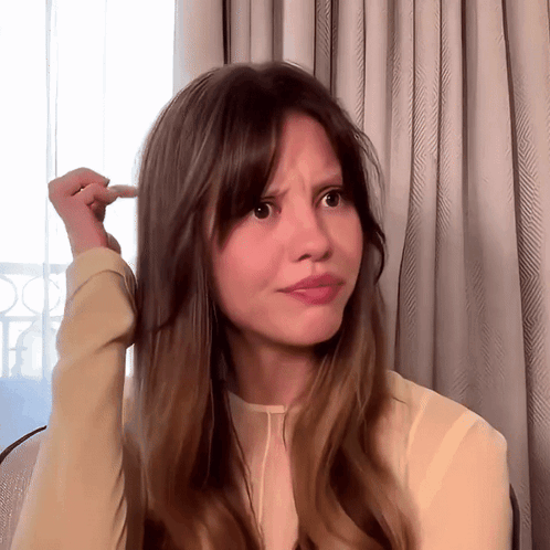 A Woman With Long Brown Hair Is Making A Funny Face With Her Finger In Her Hair GIF