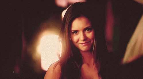 A Woman With Long Brown Hair Is Smiling And Looking At The Camera . GIF