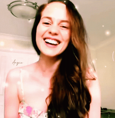 A Woman With Long Brown Hair Is Smiling With Angie Written On Her Chest GIF