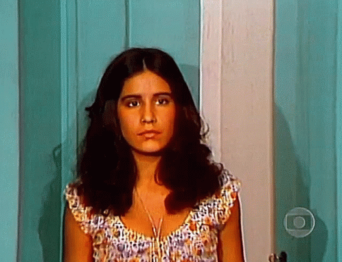 A Woman With Long Brown Hair Is Standing In Front Of A Door . GIF