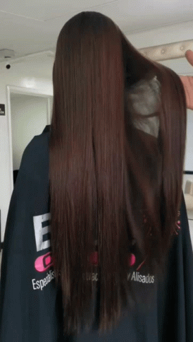 A Woman With Long Brown Hair Is Wearing A Black Cape That Says Especialistas Alisados GIF