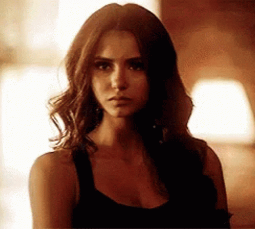 A Woman With Long Brown Hair Is Wearing A Black Tank Top And Looking At The Camera . GIF