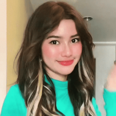 A Woman With Long Brown Hair Is Wearing A Blue Sweater And Smiling For The Camera . GIF