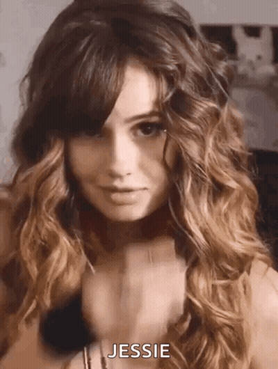 A Woman With Long Curly Hair And Bangs Is Wearing A Choker Necklace And Looking At The Camera . GIF