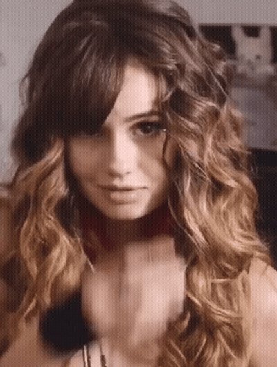 A Woman With Long Curly Hair And Bangs Is Wearing A Choker Necklace . GIF