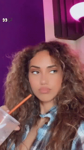 A Woman With Long Curly Hair Is Drinking A Drink With A Straw . GIF