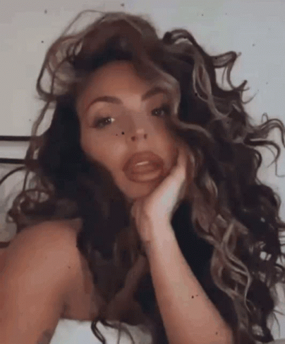 A Woman With Long Curly Hair Is Laying On A Bed With Her Hand On Her Chin . GIF