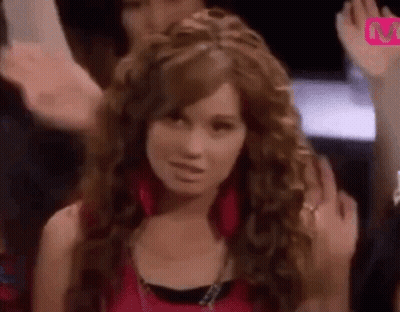 A Woman With Long Curly Hair Is Standing In Front Of A Crowd Of People . GIF