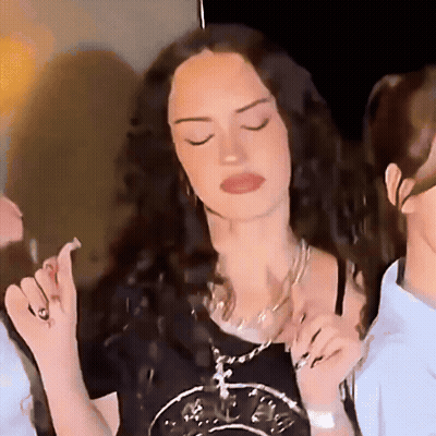 A Woman With Long Curly Hair Is Wearing A Black Shirt And A Necklace GIF