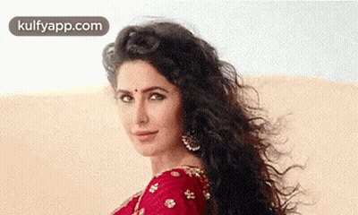 A Woman With Long Curly Hair Is Wearing A Red Saree And Earrings And Looking At The Camera . GIF