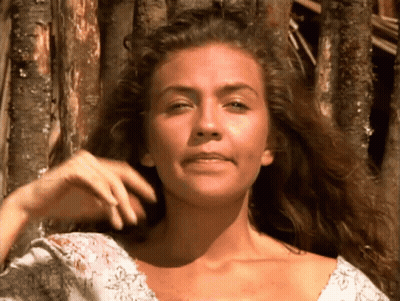 A Woman With Long Curly Hair Looks At The Camera GIF