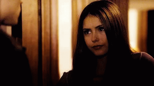 A Woman With Long Dark Hair Is Looking At A Man In A Doorway . GIF