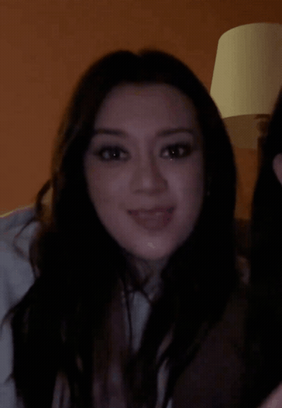 A Woman With Long Dark Hair Is Smiling And Looking At The Camera GIF