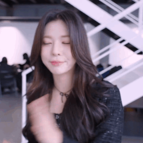 A Woman With Long Dark Hair Is Standing In Front Of A White Staircase . GIF