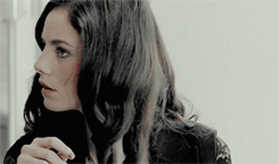 A Woman With Long Dark Hair Is Wearing A Black Lace Top And A Black Turtleneck . GIF