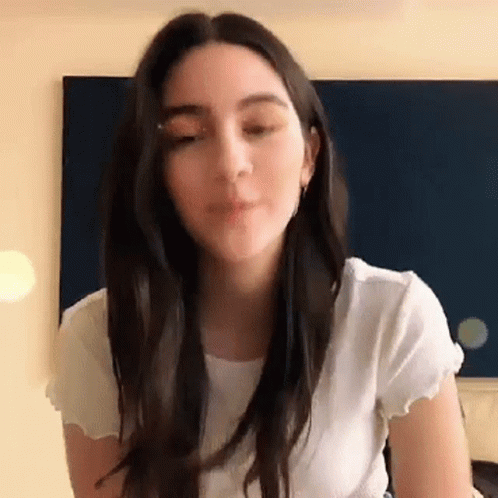 A Woman With Long Dark Hair Is Wearing A White Shirt . GIF